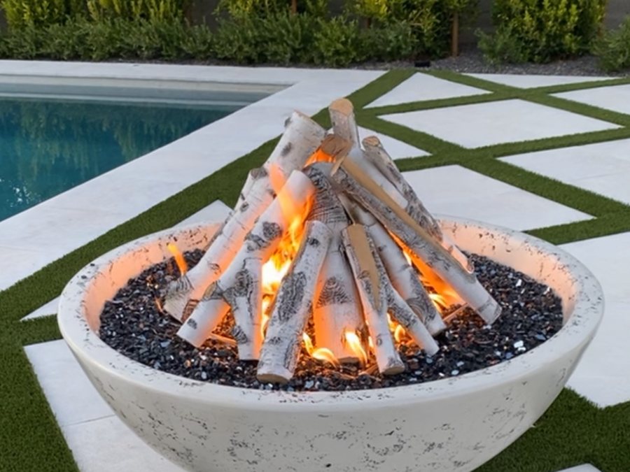 A concrete bowl fire pit burning beside a pool on a finished patio