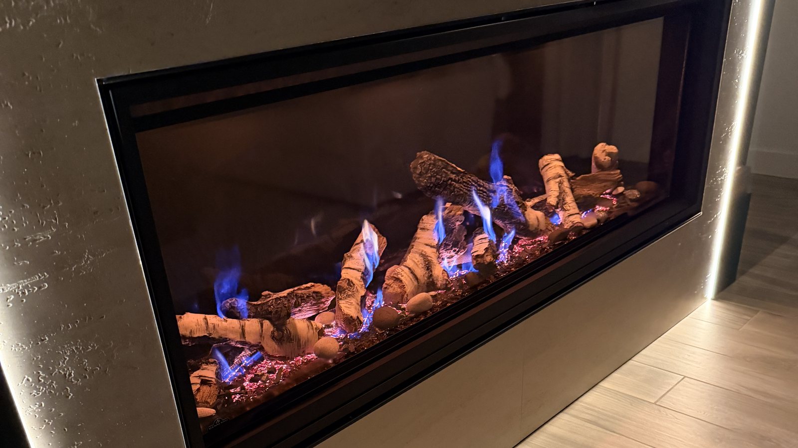 A linear gas fireplace burning in a plaster surround with cove lighting in a Mesa home