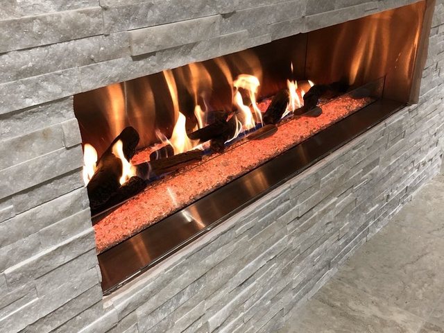 A linear fireplace burning in a stacked stone wall