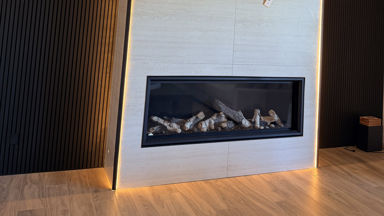 A wide linear gas fireplace built into a travertine wall with concealed cove lighting