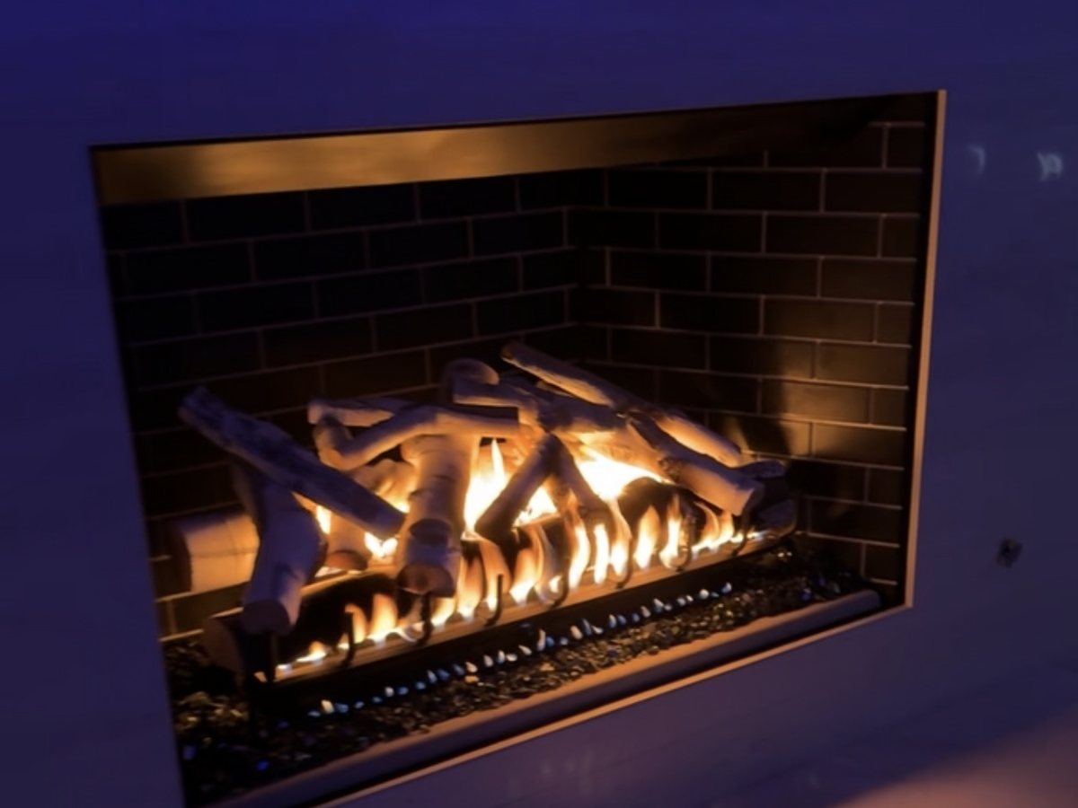A sealed gas firebox with a herringbone brick liner and a ceramic log set, burning