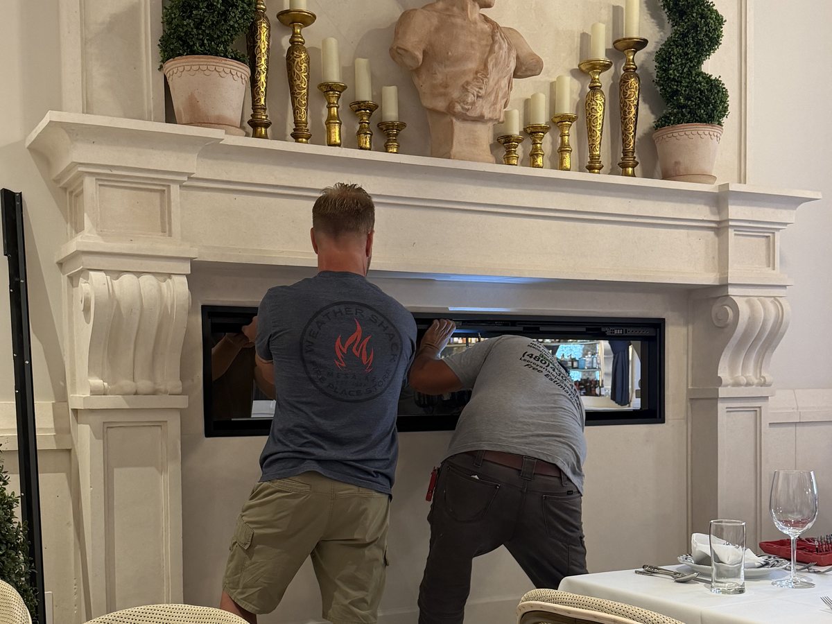 Two Weather Shack installers fitting a linear gas fireplace into a cast stone mantel