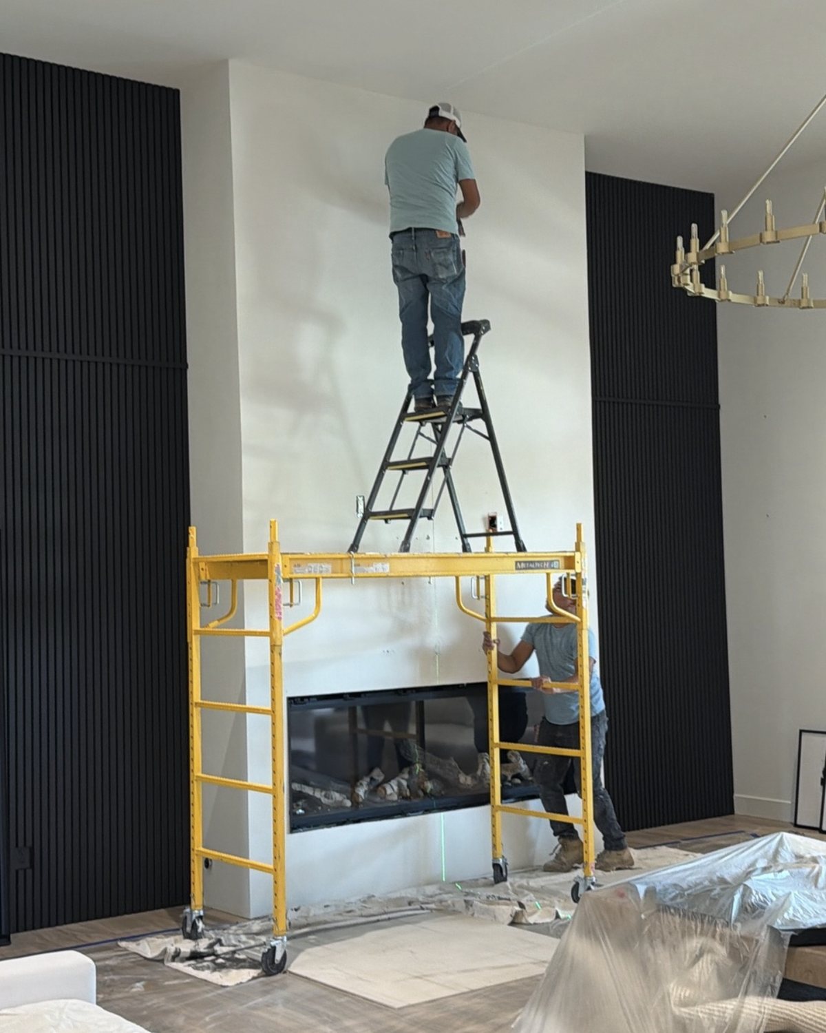 Installers on scaffolding finishing the wall above a linear fireplace