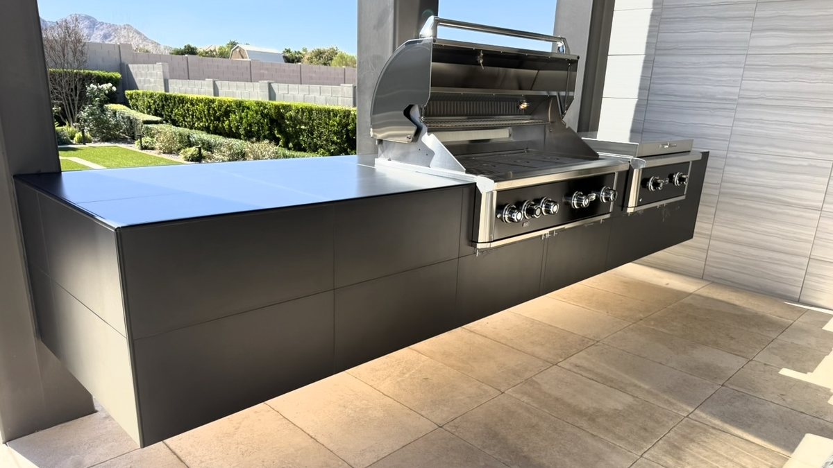 A built-in grill and side burner in a black outdoor kitchen island on a travertine patio